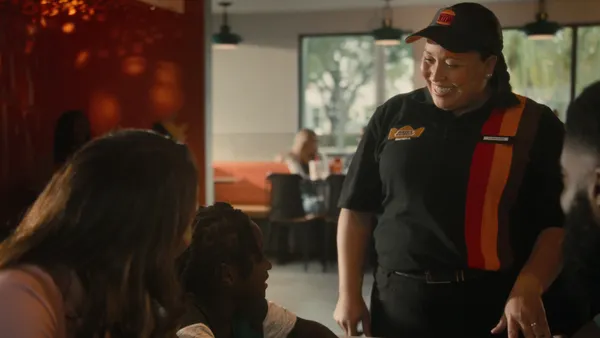 A smiling woman in a Burger King uniform at a table of restaurant guests.