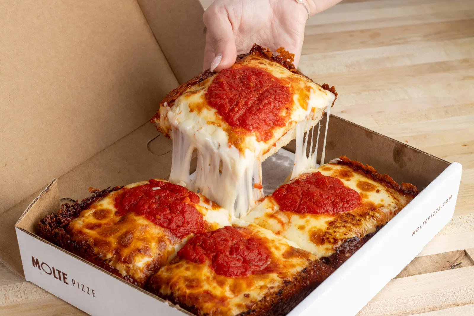 A hand holds a pepperoni Detroit-style pizza inside a white box.