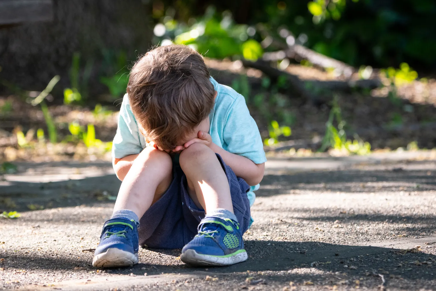 A child sits on the ground outside with their head in their hands and in their lap