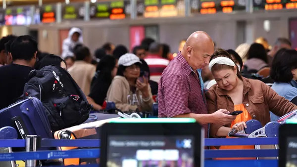 Travelers wait in line with their bags at the airport.