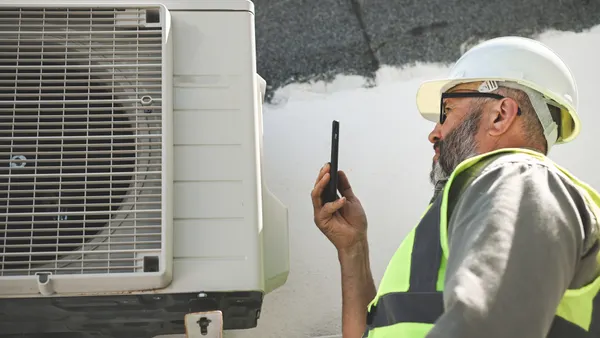 An engineer uses his phone to help repair an air conditioner.