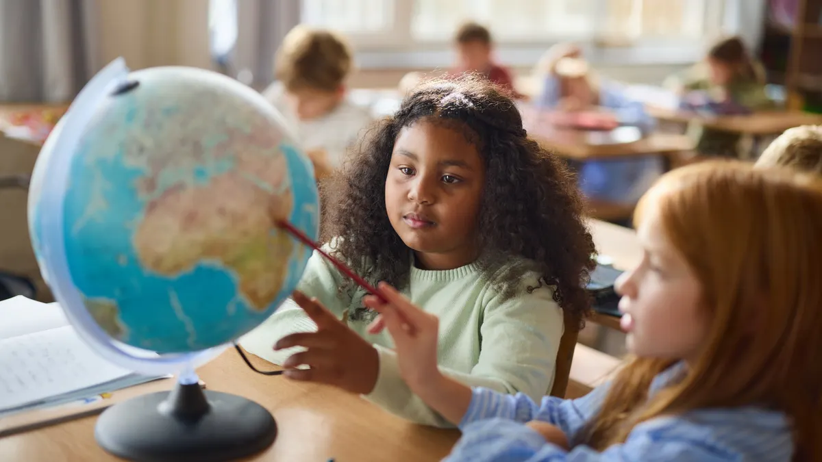 Two young girl students study a globe in an elementary school classroom.