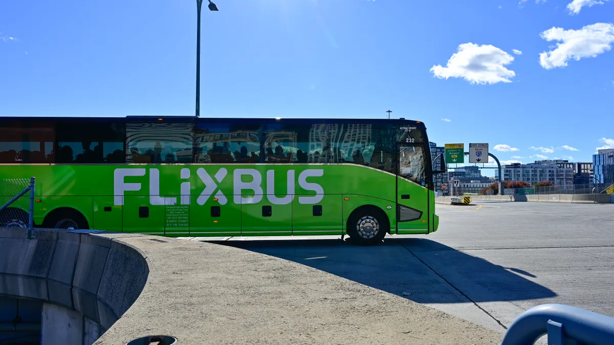 A large green motor coach crossing an intersection under a deep blue sky.