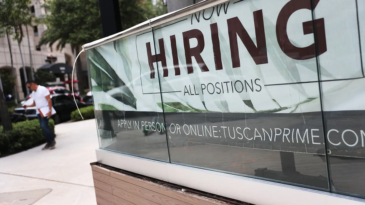 A "Now hiring" sign seen plastered on the side of an escalator.