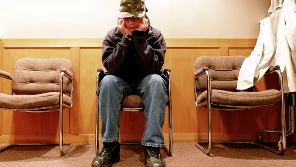 A teen boy sits outside of a high school principal's office.