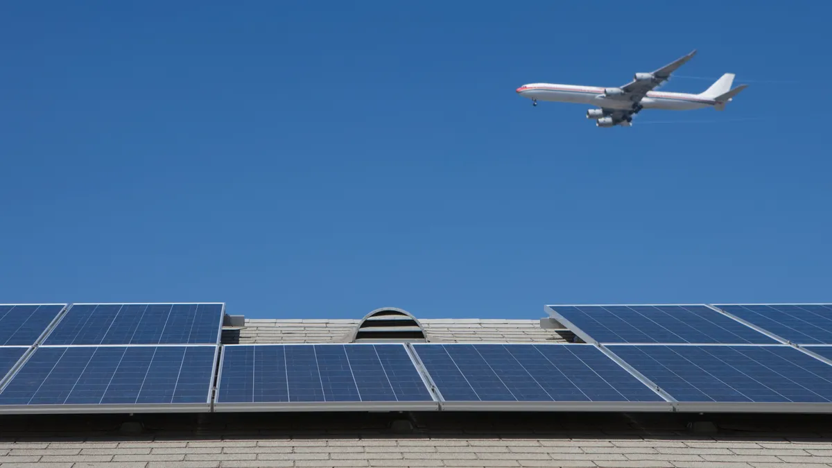 An airplane flies over a rooftop with a solar array in Los Angeles, California