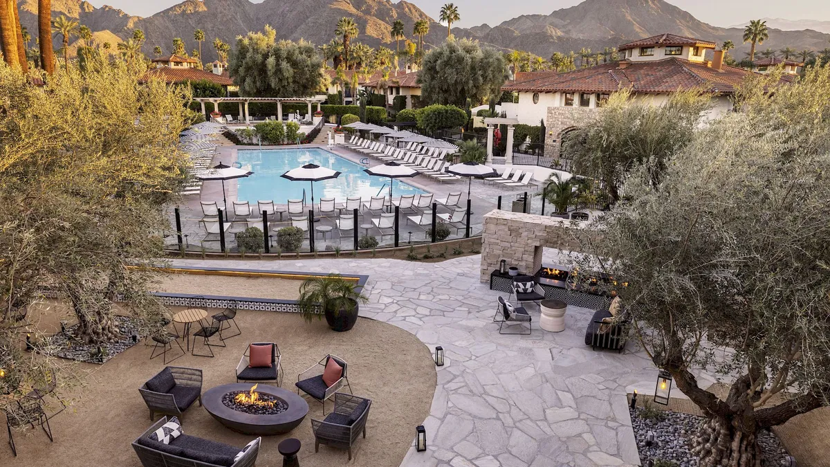 Patio furniture frames an outdoor fire next to a pool.