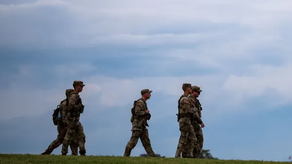Five people wearing military fatigues walking with blue sky overhead.