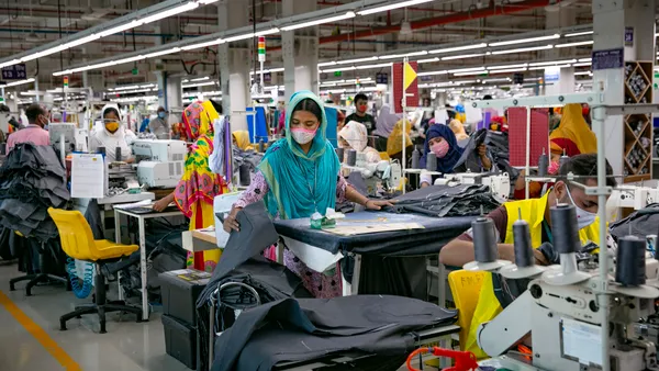 A factory with rows of Bangladeshi garment workers behind their sewing machines working on fashion garments