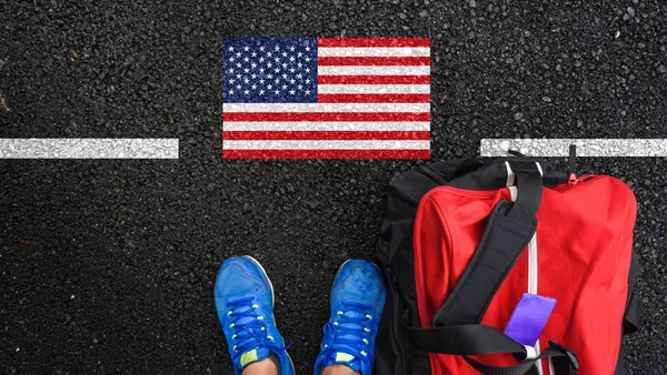 Someone's sneakers stand next to a duffle bag and an American flag drawn on the pavement.