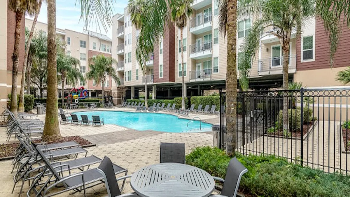 Palm trees, deck chairs and apartments surrounding a pool.