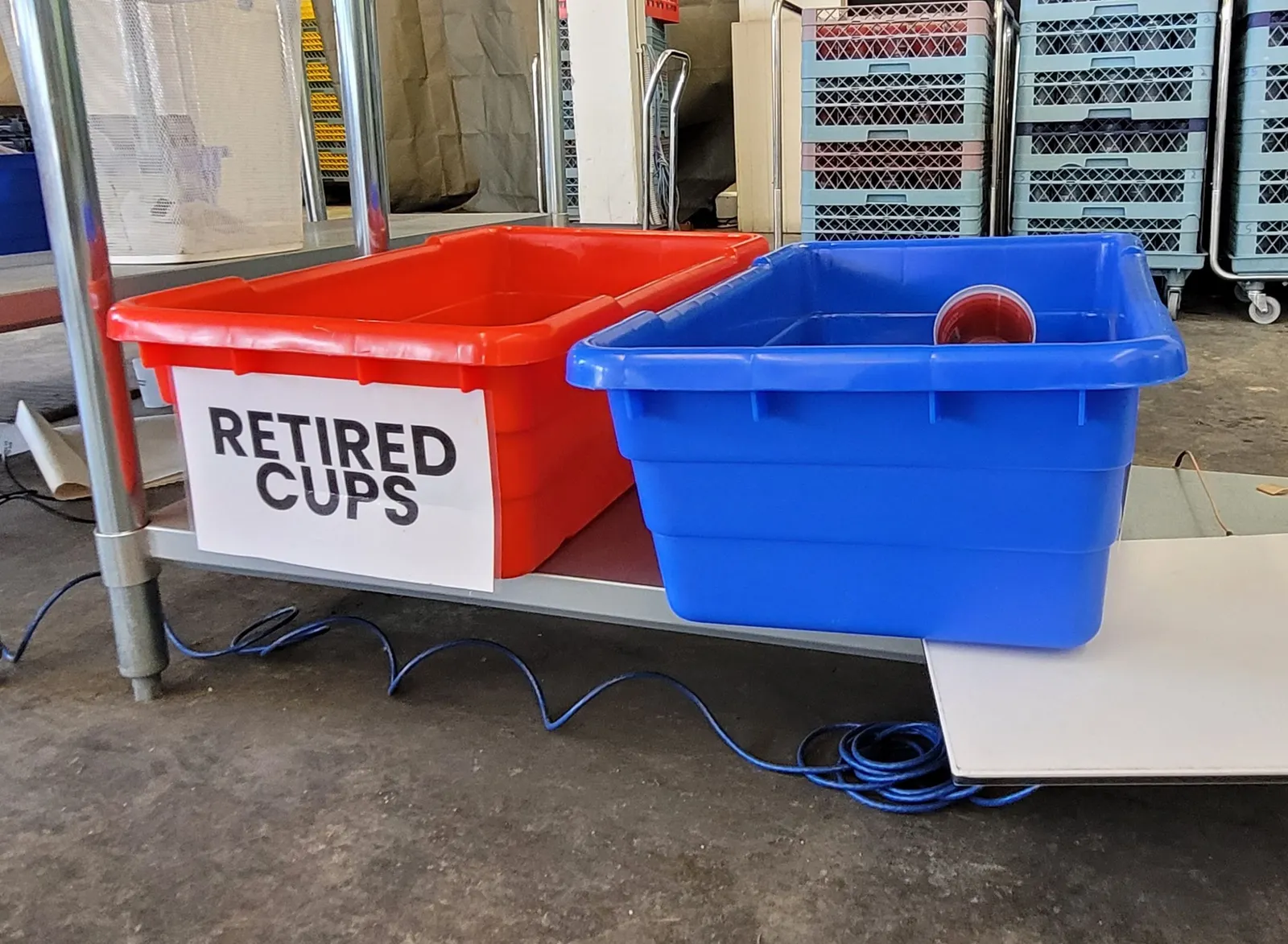 A red bin with a sign that says "retired cups" sits next to a blue bin in an industrial setting.
