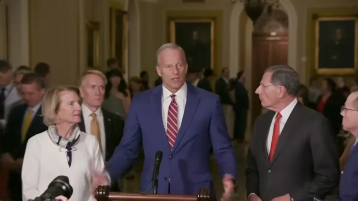 Person in blue suit at a podium surrounded by people beside and behind.