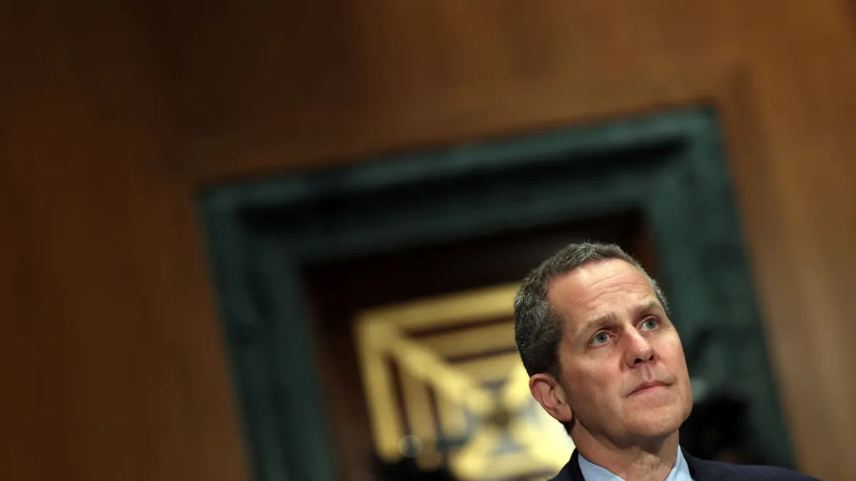 Michael Barr is shown in the lower right corner, sitting behind a microphone, in a wood paneled Congressional room.