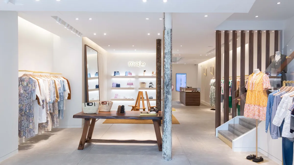 Interior view of a Maje store shows wood beams, pale concrete floors and racks of dresses.