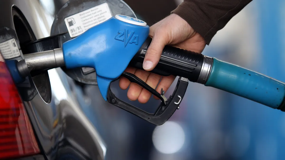 A photo of a hand holding a gas pump nozzle as the person pumps gas into a motor vehicle.