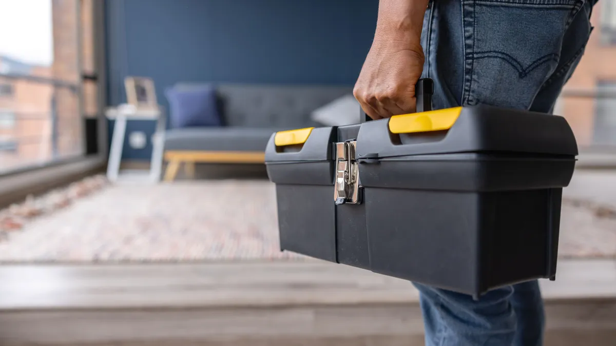 a maintenance worker carries a toolbox into an apartment