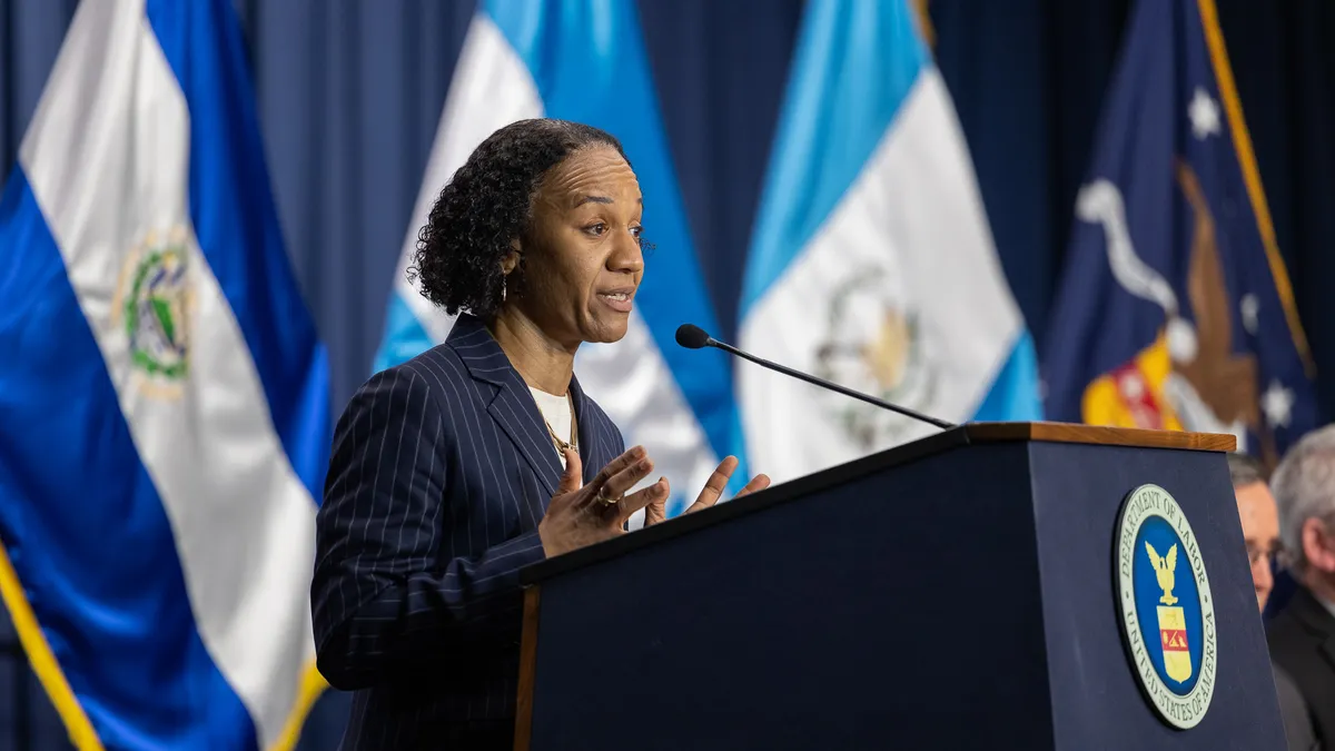 A woman in a suit stands at a podium with a Department of Labor seal on it, speaking.