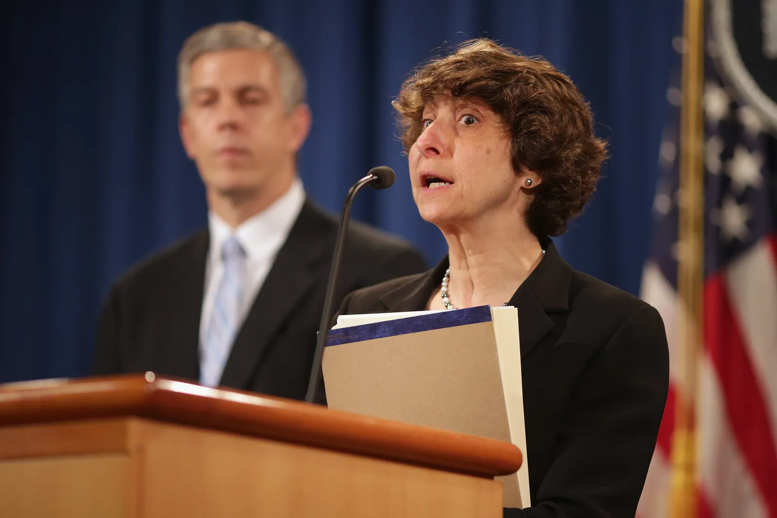 Two people stand at a podium with a U.S. flag in the background.
