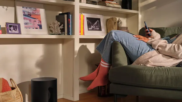 A person looks on their phone lounging on the couch with a Sonos Mini in the foreground.