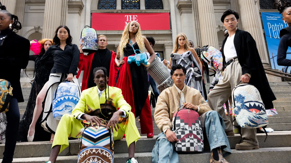 Models sit on the steps of the Metropolitan Museum of Art in New York holding handbags featuring artwork.