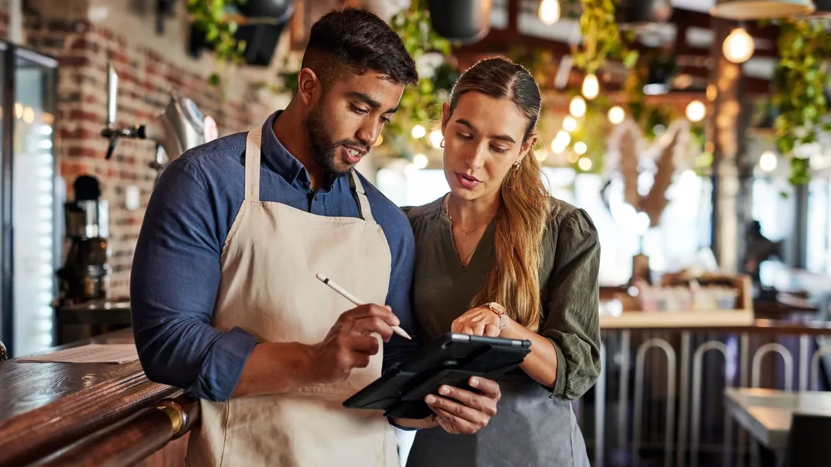 Two workers in a restaurant collaborating on a tablet.