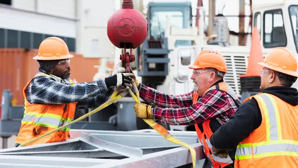 A group of construction workers positions a crane hook.