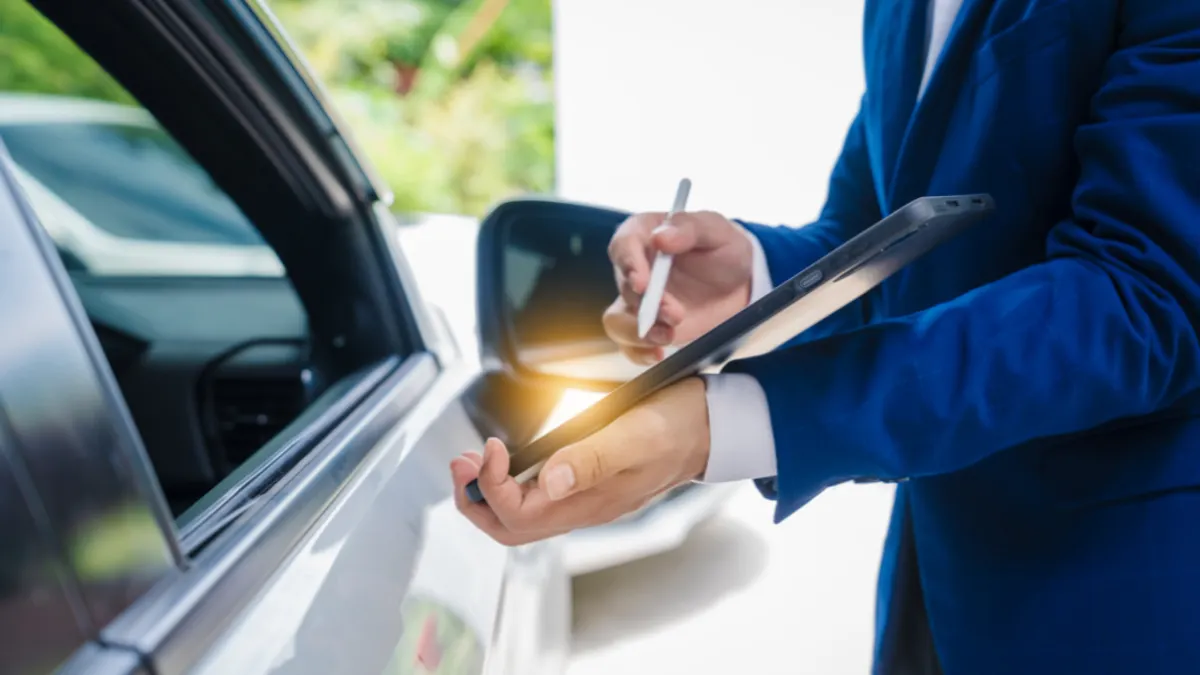 Person holding tablet while standing next to a car.