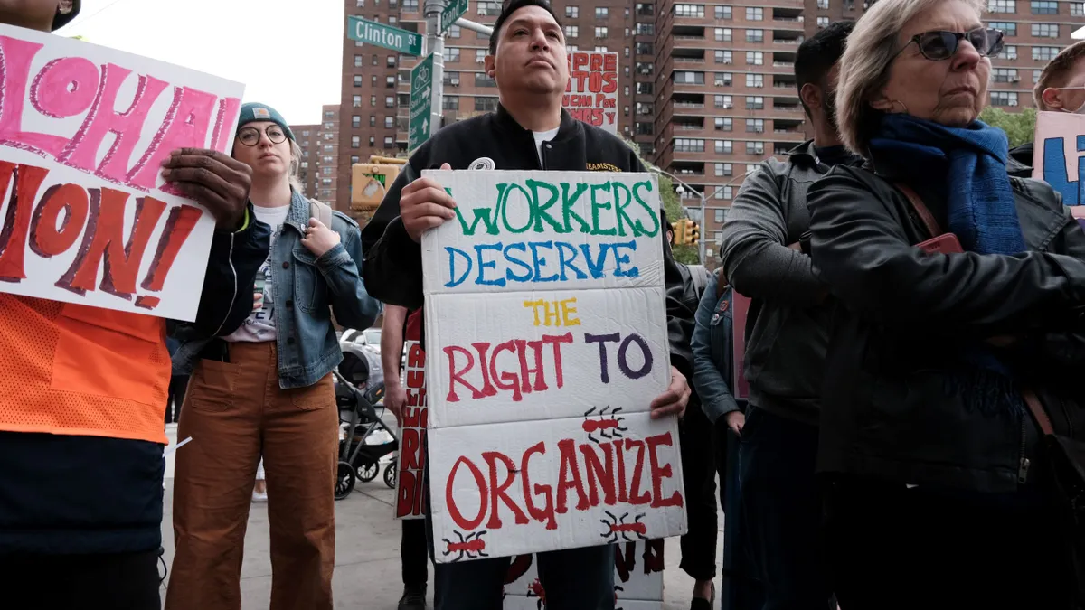 A individual holds a sign that says "workers deserve the right to organize."