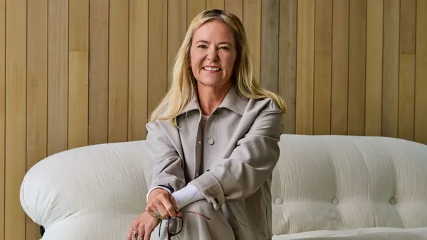 Heidi O'Neill sits on a bench in front of a pale wood wall.