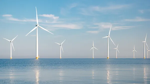 Offshore wind turbines are seen standing in the ocean against a blue sky.