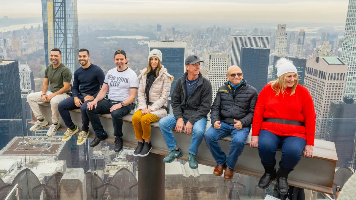 Image of seven people sitting on a beam with New York City in the background.