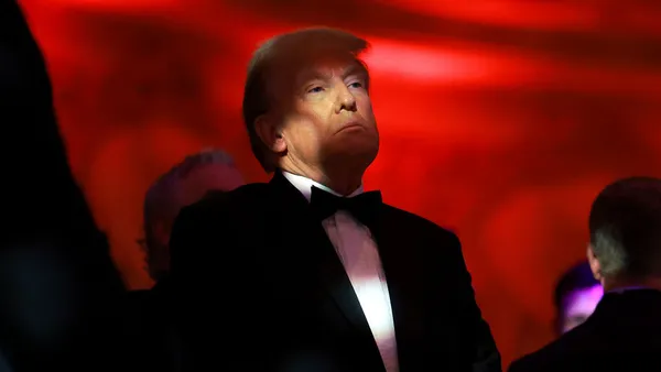 Donald Trump stands against a red backdrop with a shadow over his face