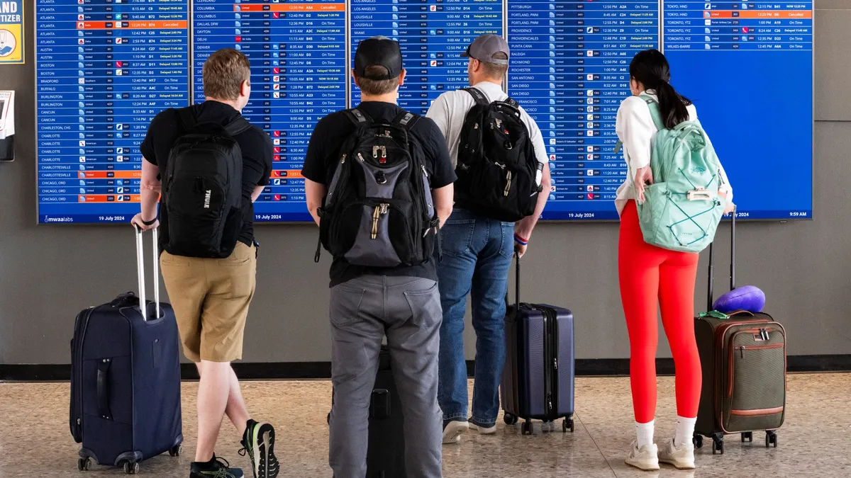 People stand in front of a screen showing flight arrivals and departures.