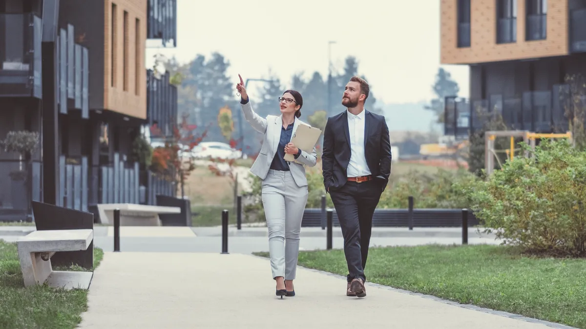 Real estate agent and customer walking between apartment buildings.