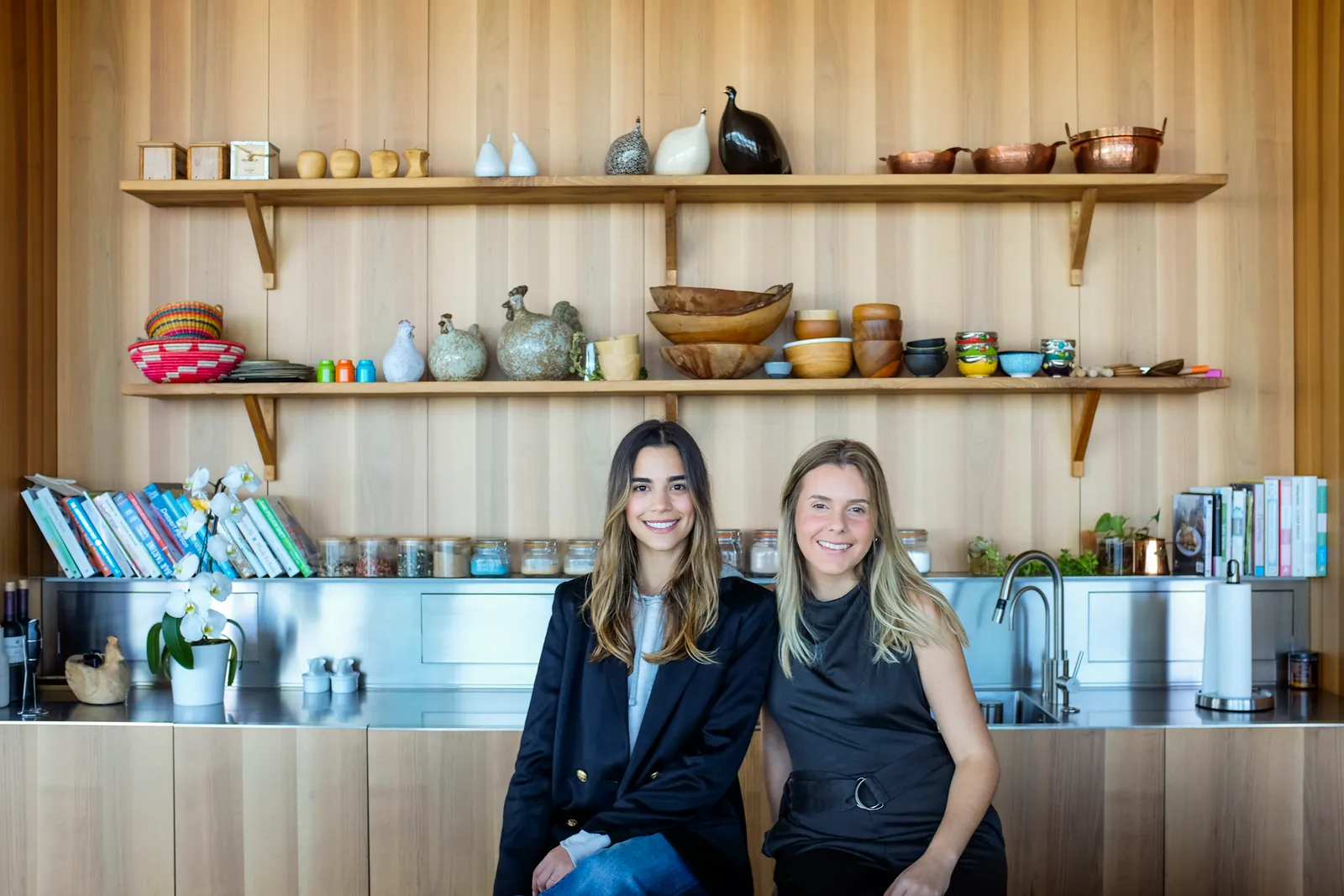 Two women dressed business casual sitting in a wood paneled kitchen