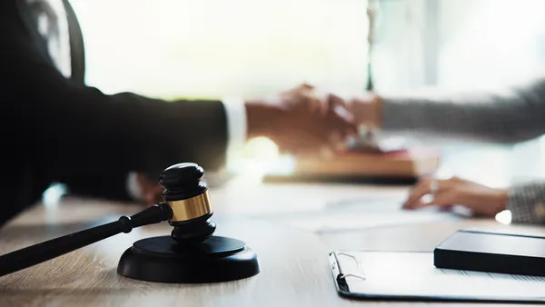 Two people in business attire shake hands, with a gavel in the foreground.