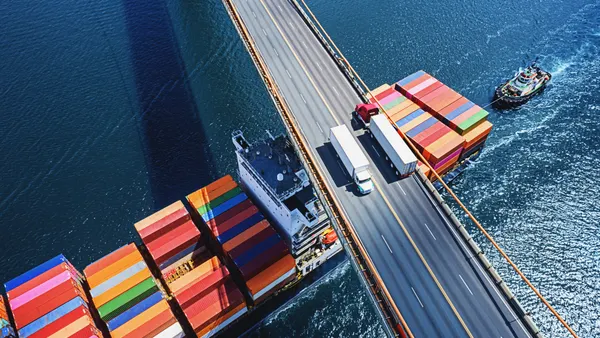 Trucks cross a bridge as a container ship passes underneath.