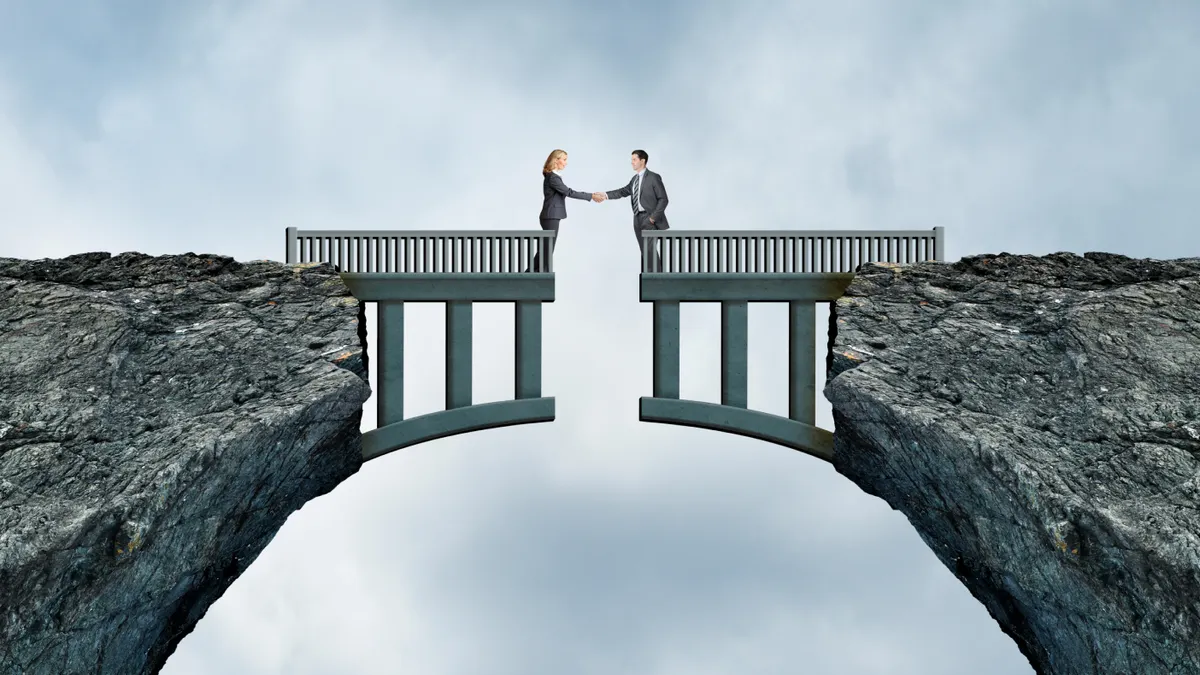 A man and a woman shake hands as they stand on opposite sides of a bridge separated by a missing gap.