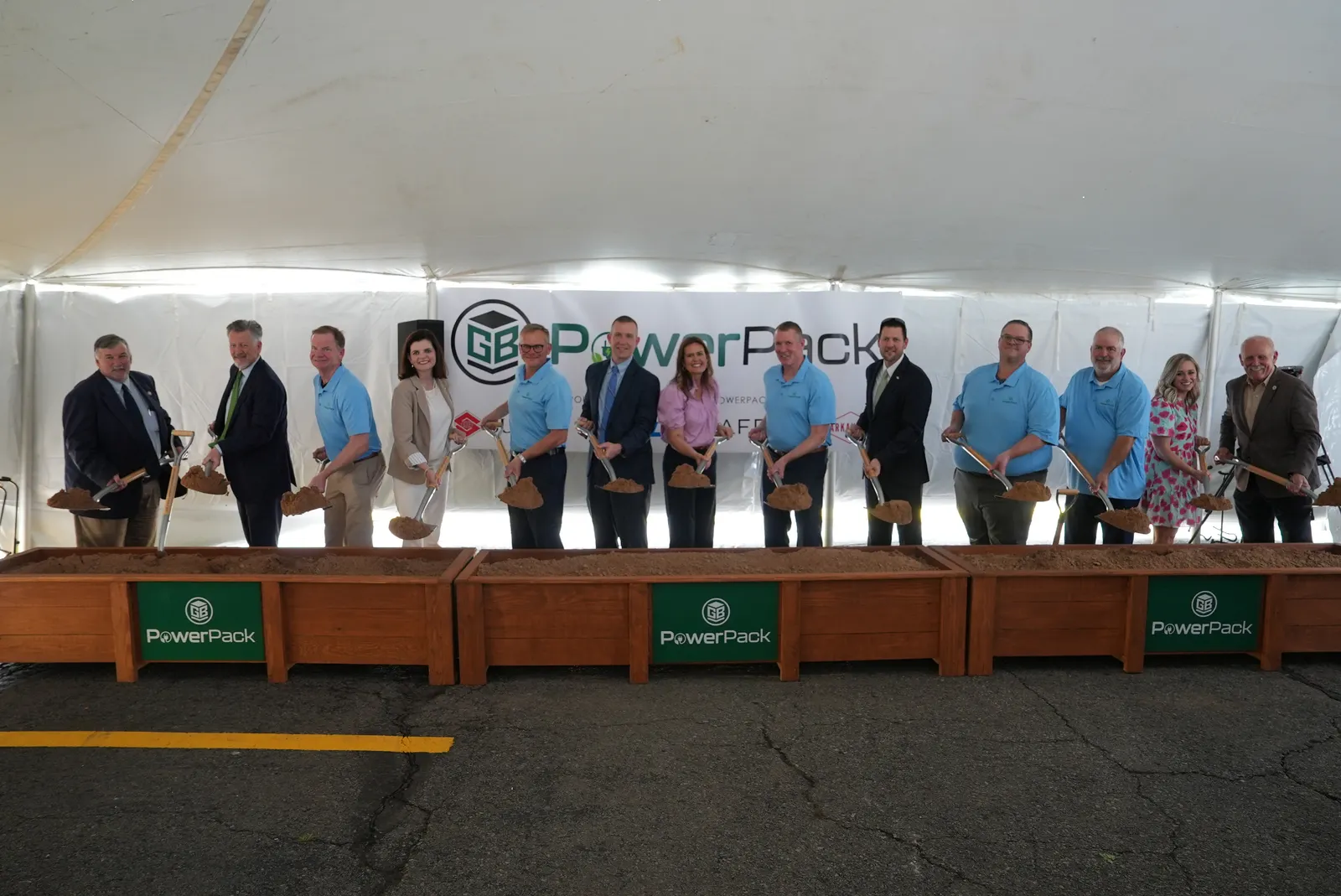 Thirteen people hold shovels with dirt at a groundbreaking ceremony.
