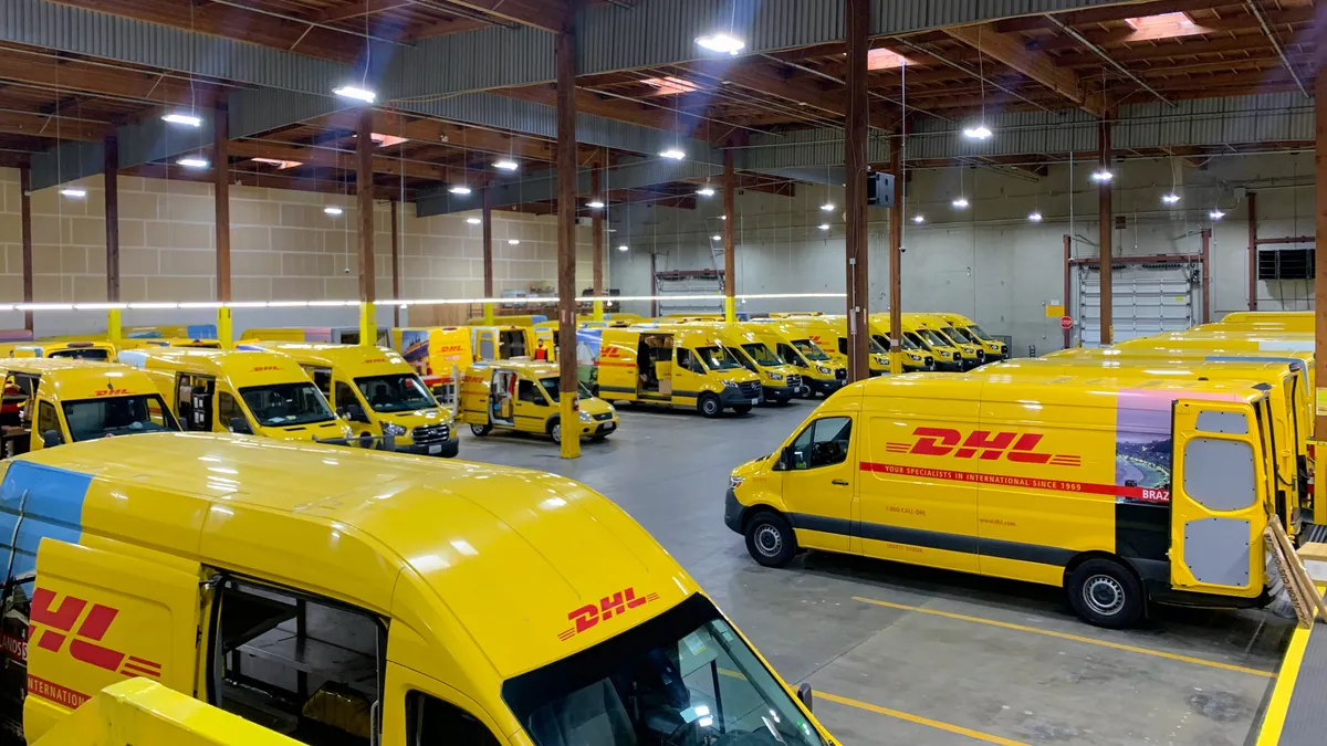 A fleet of DHL-branded yellow trucks are parked in a warehouse.