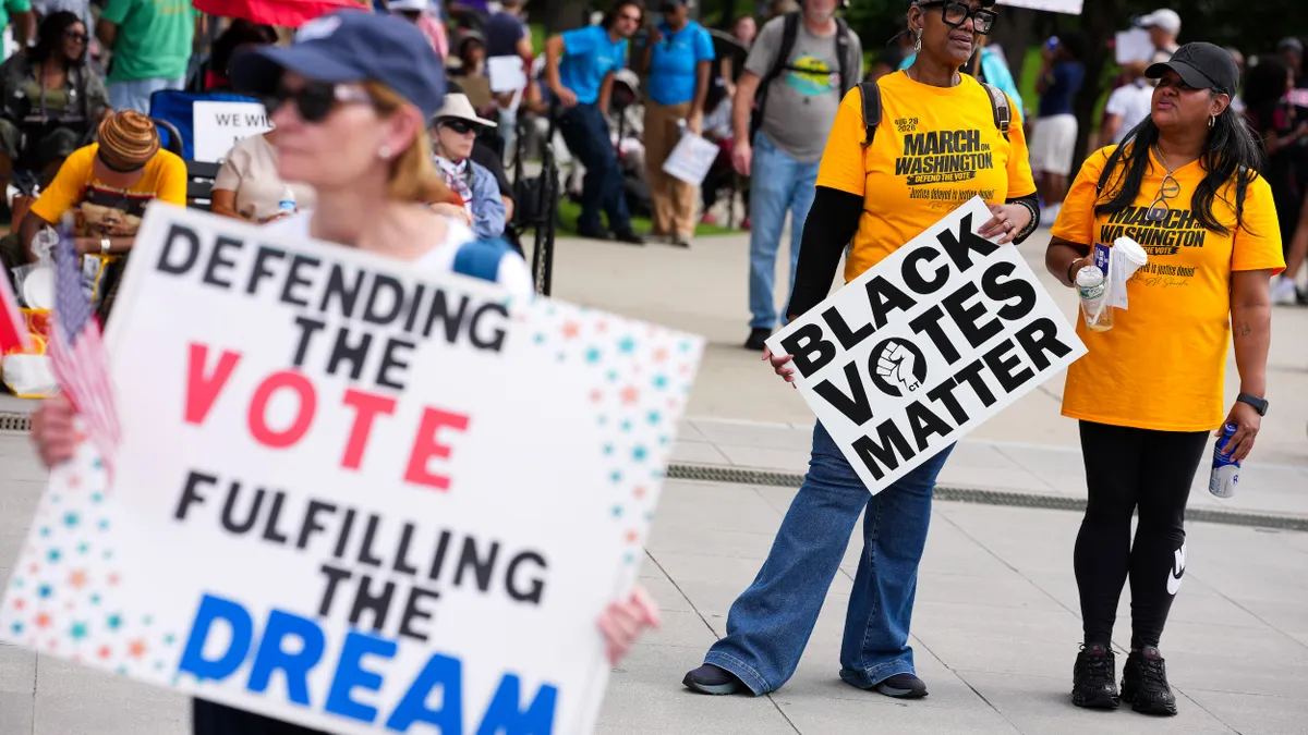 People at a protest holding signs that say "Defending the Vote, Fulfilling the Dream" and "Black Votes Matter"