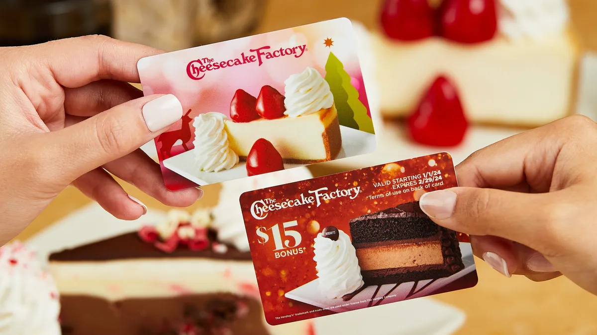 Two hands holding up gift cards from Cheesecake Factory