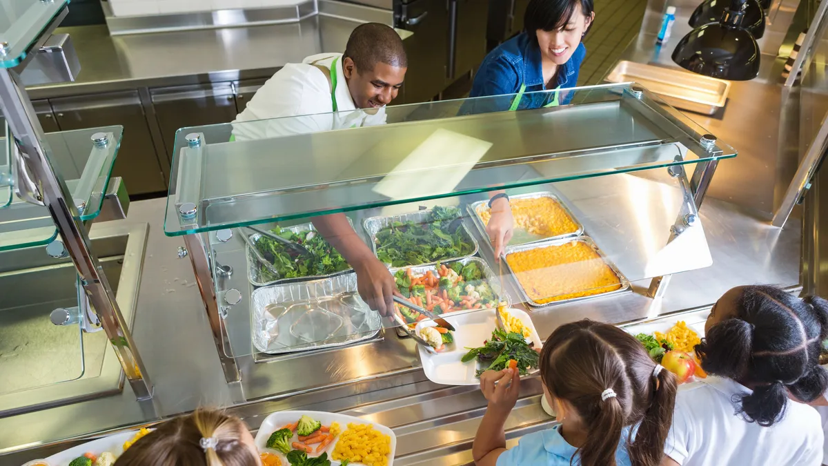 Two school foodservice employees serve food to students in line at a cafeteria.