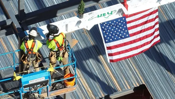 Construction workers work in a lift next to an American flag.