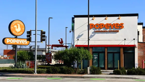 A daytime photogrpah of a white building that has an orange sign that says Popeyes Louisina Kitchen