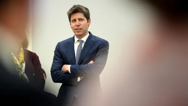 A person wearing a suit and tie stands with arms crossed.