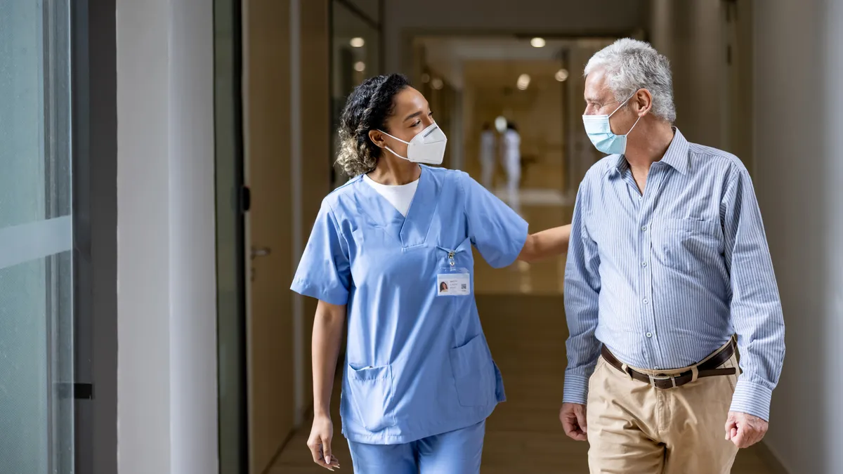 A doctor talks to a patient in the corridor of a hospital while wearing face masks.