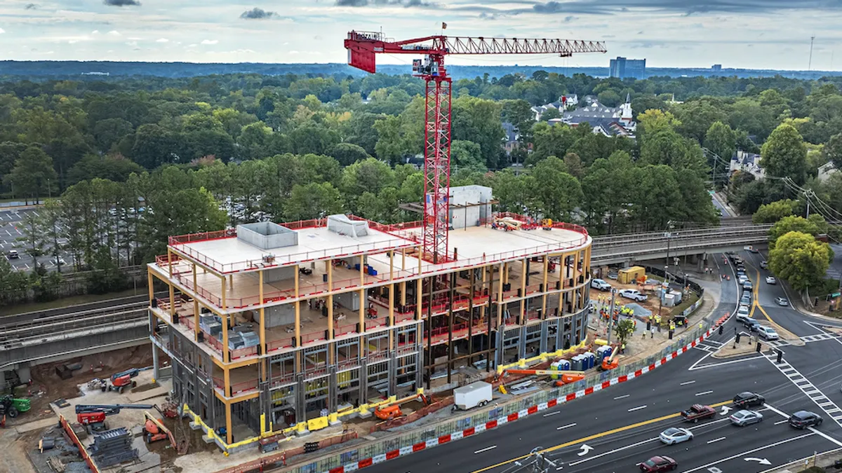 An aerial view of a building under construction. The jobsite is cordoned off, and a crane rises through the middle of the structure.