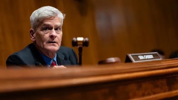 A person holds a gavel while sitting in front of a blurred out sign that says "Sen. Cassidy."